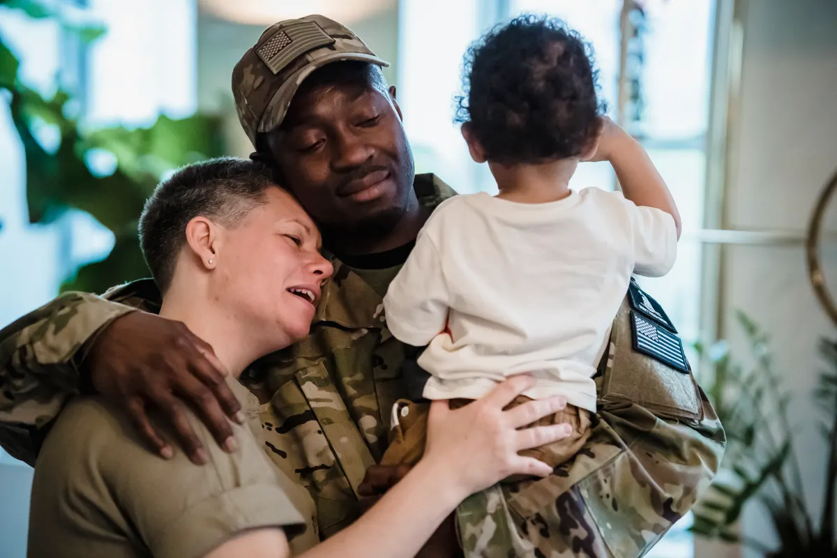 A family embracing at home, with one parent in camouflage